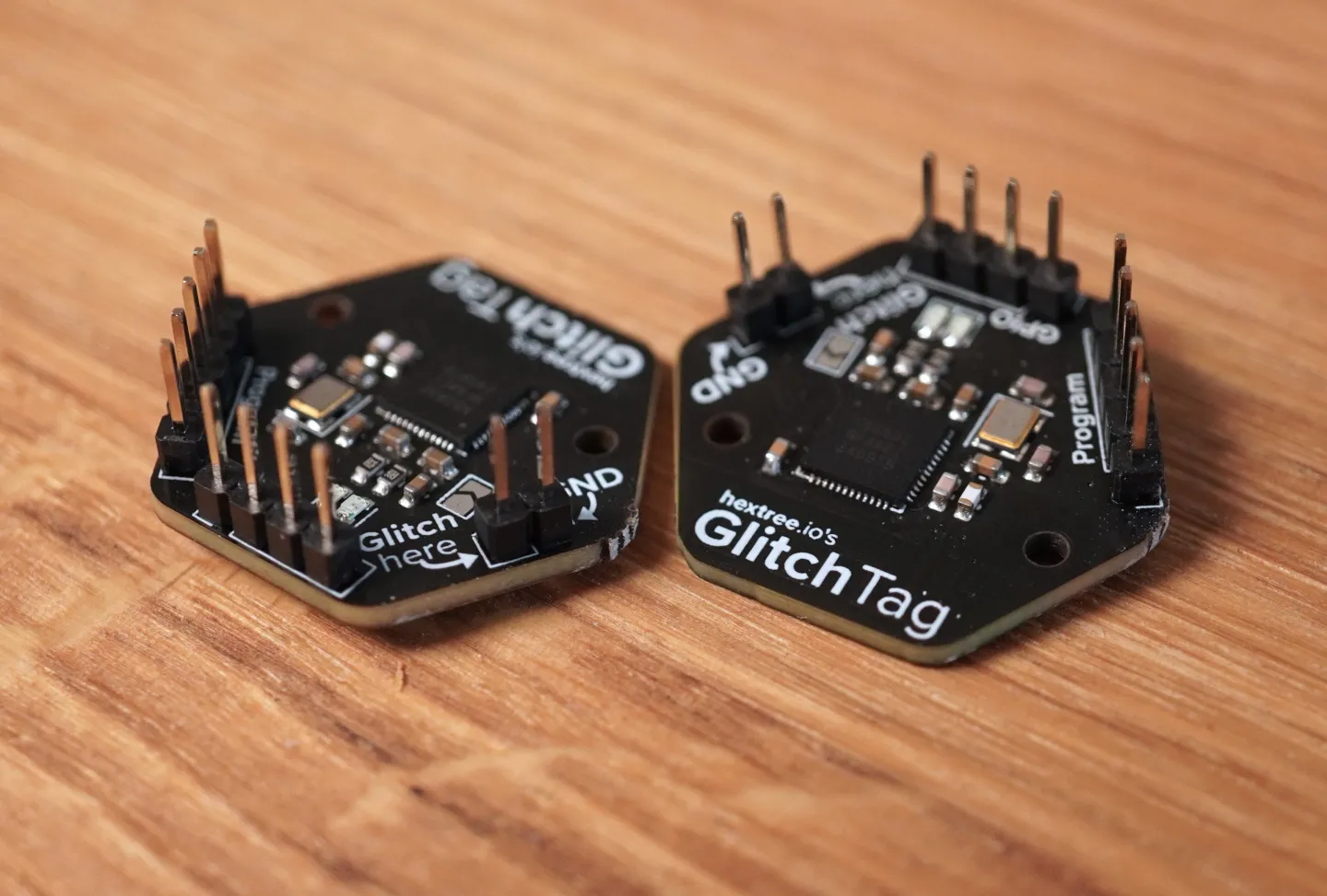 Two black hexagonal Glitch Tag boards with chips and accessible pin headers